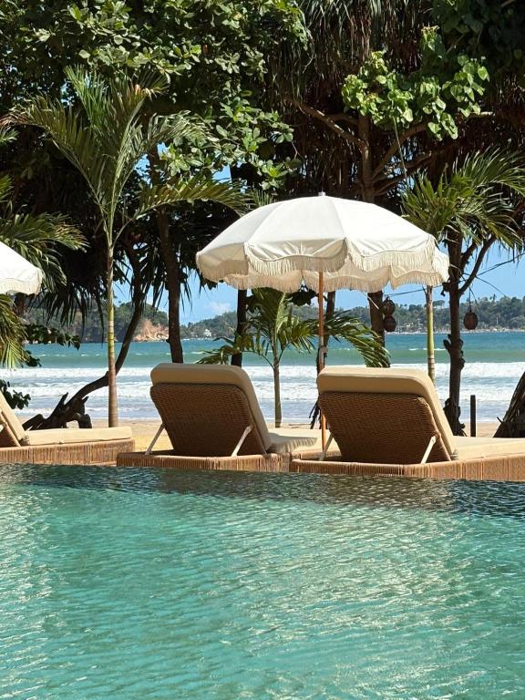 a swimming pool with chairs and umbrellas on a beach at Southbeach Weligama in Weligama