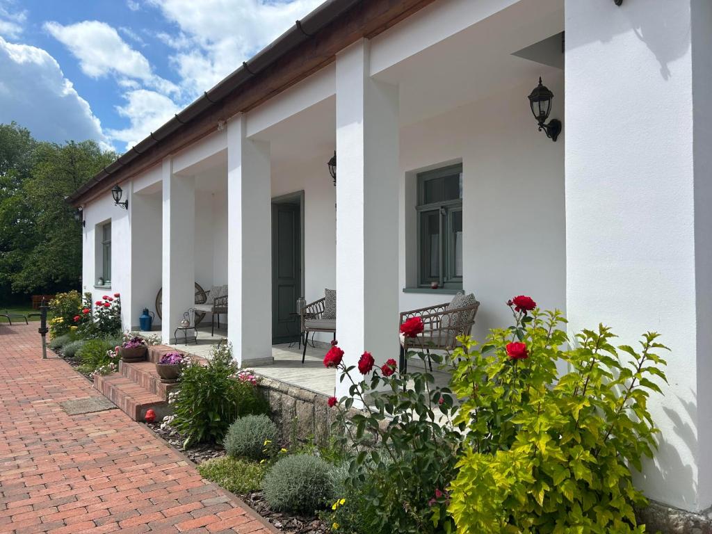 a white house with red flowers and a brick sidewalk at Relaxxa Apartman in Noszvaj