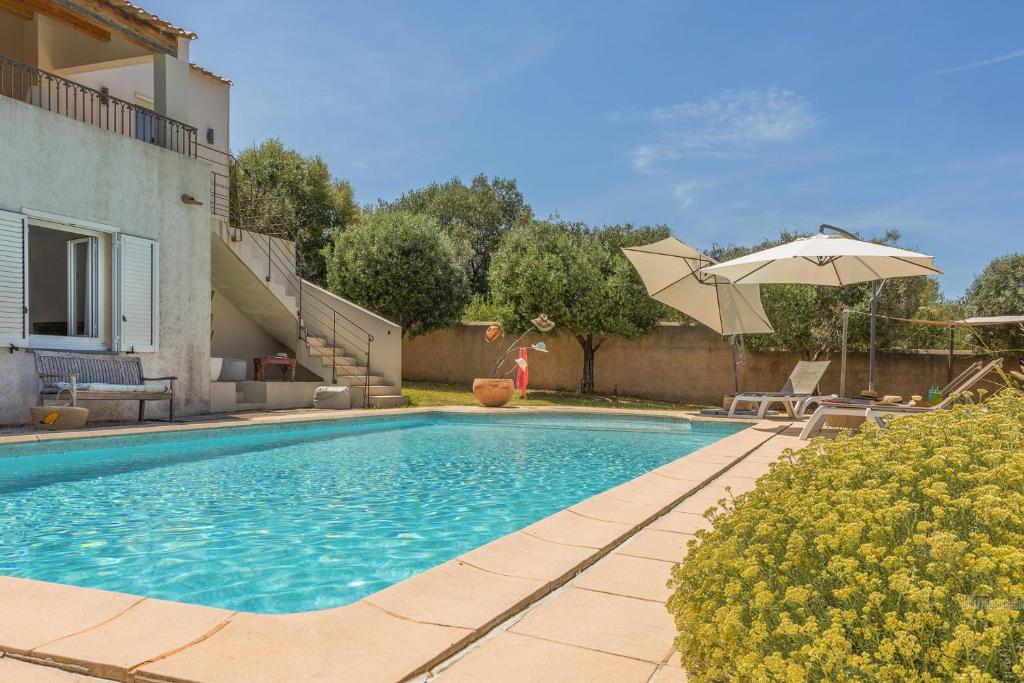 a swimming pool with an umbrella next to a house at Villa Bollaccia - piscine privée proche de la mer in Aregno