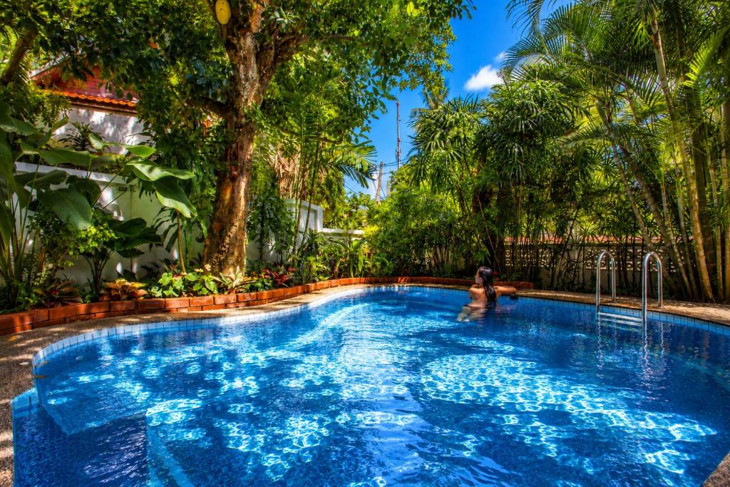 a person swimming in a blue pool with trees at Tropical Family Retreat near Ya Nui Beach - Villa Nikkie in Nai Harn Beach