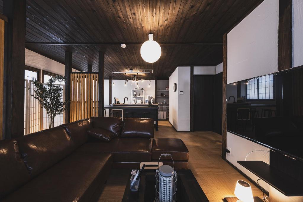 a living room with a brown leather couch and a kitchen at Hidasumika Ojin AN in Takayama