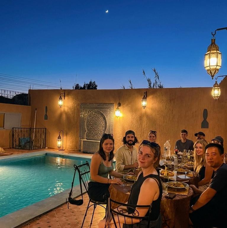a group of people sitting at a table by a pool at La Baraka Auberge in Aït Benhaddou