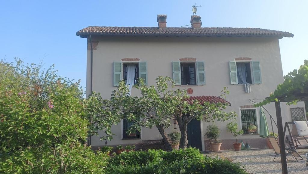 a white house with green shuttered windows and trees at La Canonica della Merella B&B in Novi Ligure