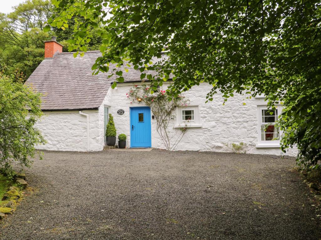a white stone house with a blue door at Rosslare Cottage in Broughshane