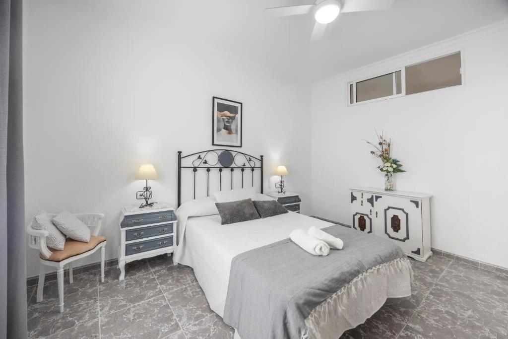 a white bedroom with a bed and a chair at En la Gloria in Barbate
