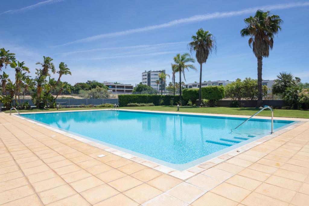 a large swimming pool with palm trees in the background at Parque Atlântico Apartment in Quarteira