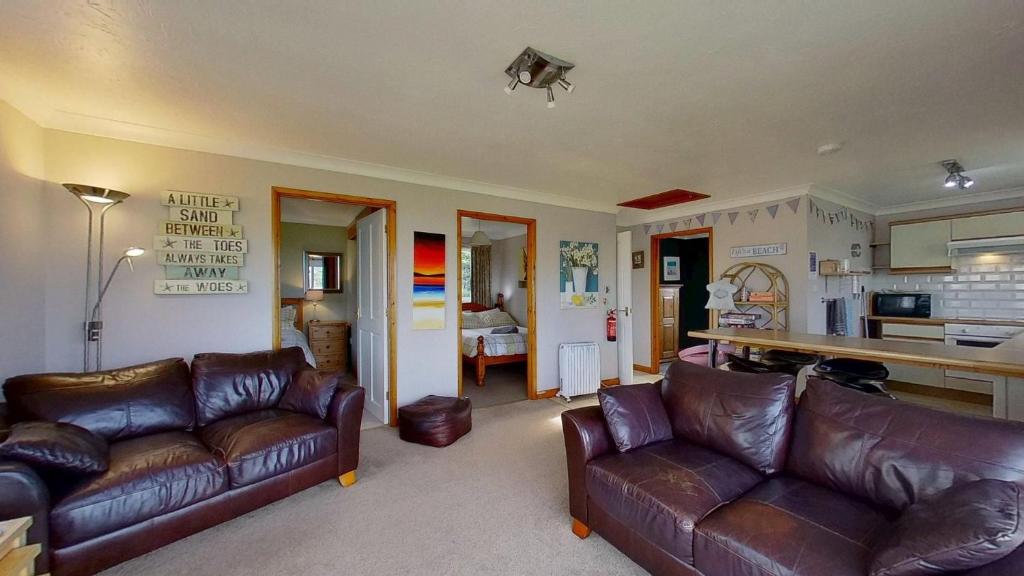 a living room with two leather couches and a kitchen at F72 Chyreden, Riviere Towans in Hayle