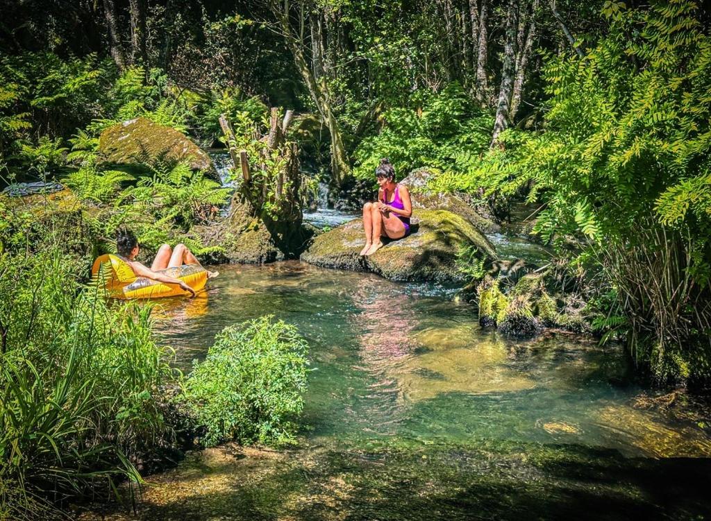 two people are sitting on rocks in a stream at Wylde Roots River House - with natural river swimming pools in Couto de Baixo