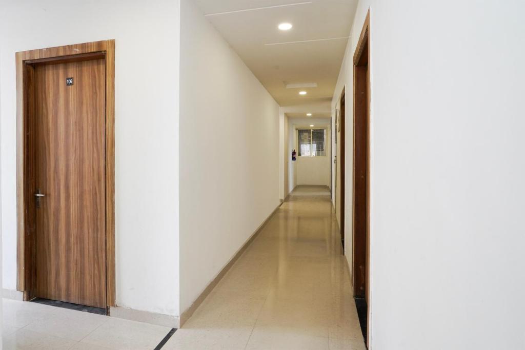 a hallway with white walls and a wooden door at Hotel O Noida Sky Suites Sector 44 Near botanical metro in Badarpur