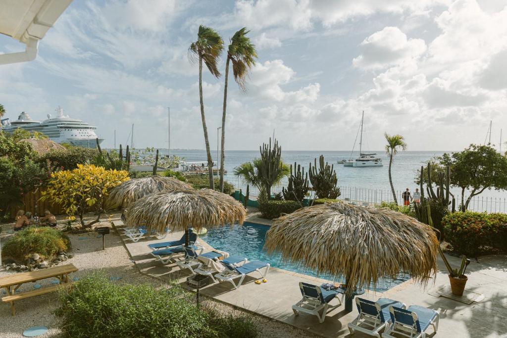 a pool with chairs and umbrellas and a cruise ship at Bonaire Oceanfront Apartments in Kralendijk