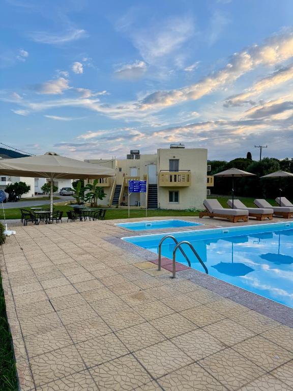 a pool with tables and umbrellas in front of a building at Angelos Studios in Kos