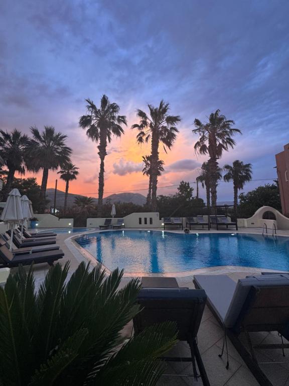 a pool with palm trees and a sunset in the background at Sun Rise Hotel Apartments in Eretria