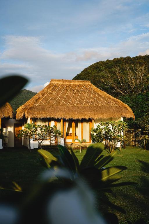 a hut with a straw roof on a field at Muara Surf House - Yoyos beachfront in Sekongkang