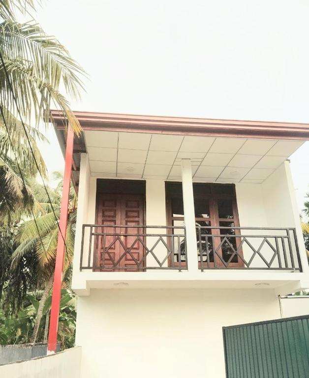 a white building with a balcony with a palm tree at Paragone Home Stay Modern 3BR Apartment Style Home AC 5 Min to Enderamulla Station 15 Minute Train Ride to Colombo in Wattala
