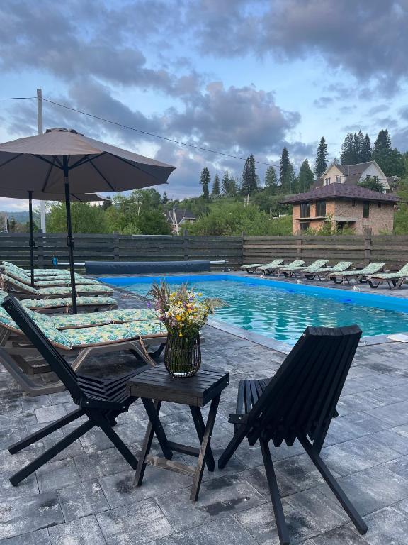 two chairs and an umbrella next to a pool at котедж петриківка З червня басейн з підігрівом 10 на 5 метрів in Slavske