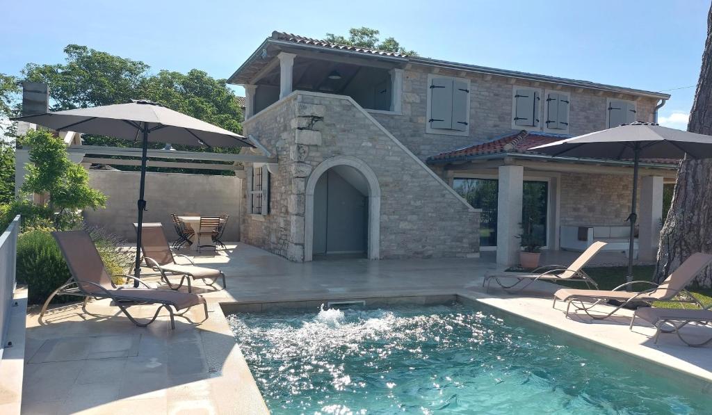 a pool with chairs and umbrellas in front of a house at VILA ŠKARLANIJA, Umag in Umag