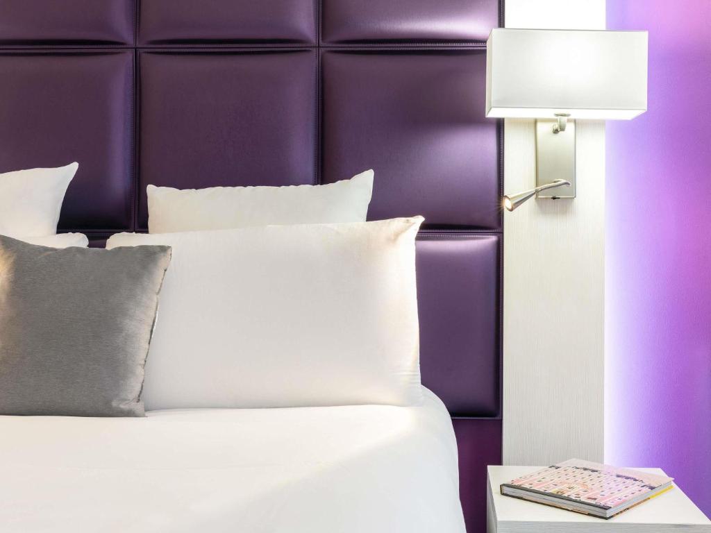a white bed with a purple headboard and a lamp at Mercure Strasbourg Aéroport in Ostwald