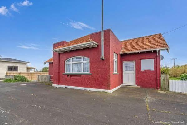 a red house sitting in a parking lot at Ruawai Post Office Accommodation in Ruawai