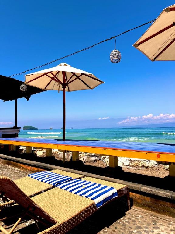 a beach with chairs and umbrellas and the ocean at Ashyana Candidasa Beach Resort in Candidasa
