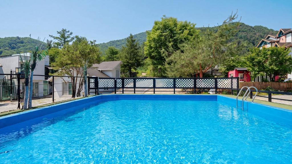 a blue swimming pool with a fence and trees at Gapyeong Shiny Pension in Gapyeong