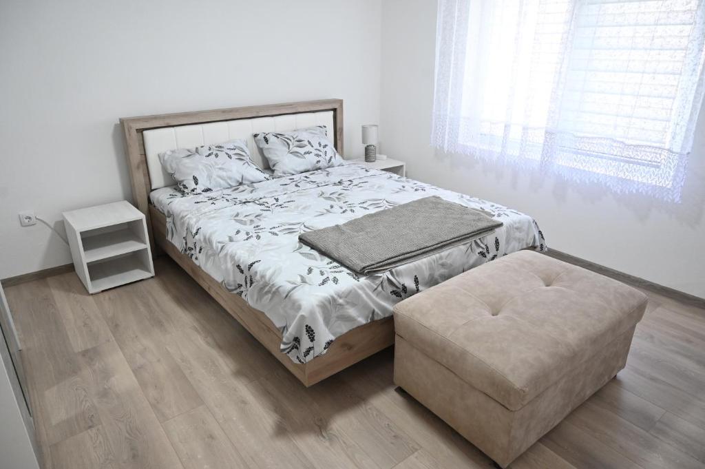 a white bedroom with a large bed and a stool at Apartman biserna Sofija in Topola