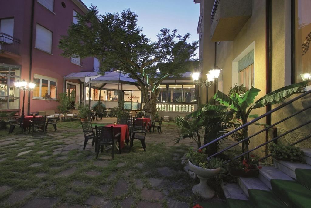 un patio al aire libre con mesas, sillas y un árbol en Hotel Flora, en Cesenatico