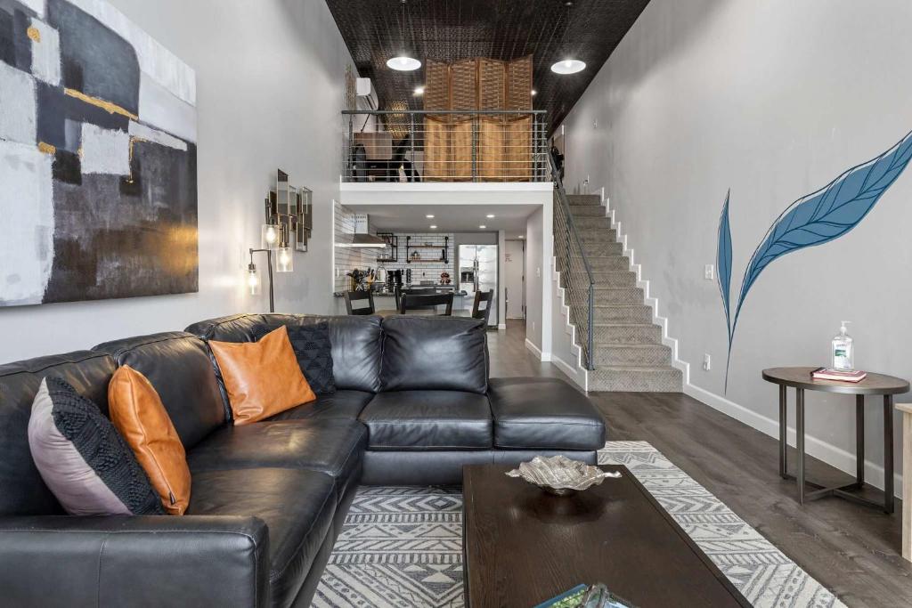 a living room with a black leather couch and stairs at Industrial-Chic Loft-King Bed & Natural Light in Wheat Ridge
