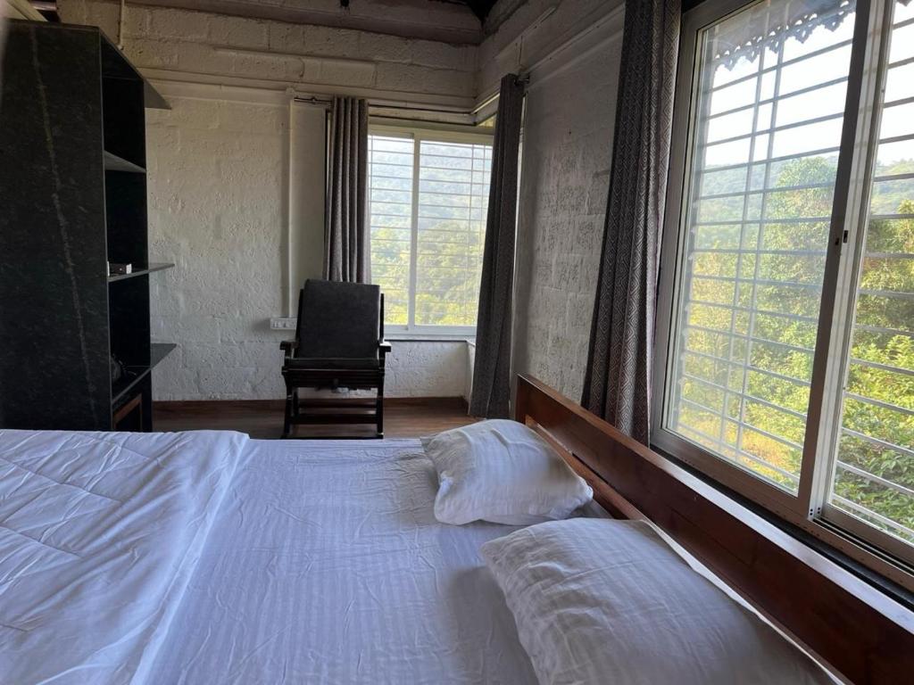 a bedroom with a bed and a chair and windows at Nature's Abode in Pune