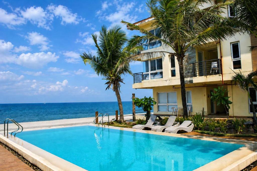 a swimming pool in front of a building with the ocean at Brisa Marina Beach Resort powered by Cocotel in Morong