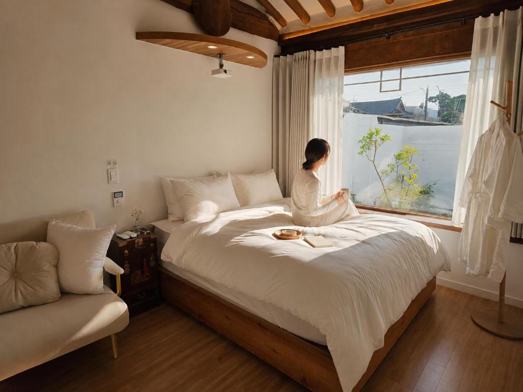 a woman sitting on a bed looking out a window at 한옥스테이 설화 in Gyeongju