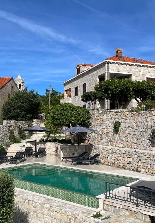 a villa with a swimming pool in front of a stone wall at Apartments Kralj Ana in Cavtat