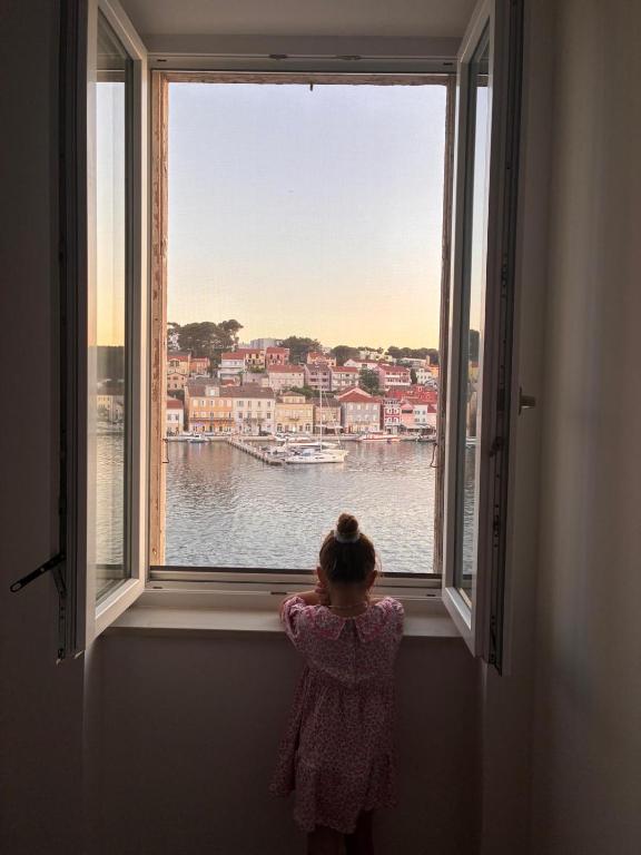 a little girl looking out a window at the water at Ridzak Riva Rooms in Mali Lošinj