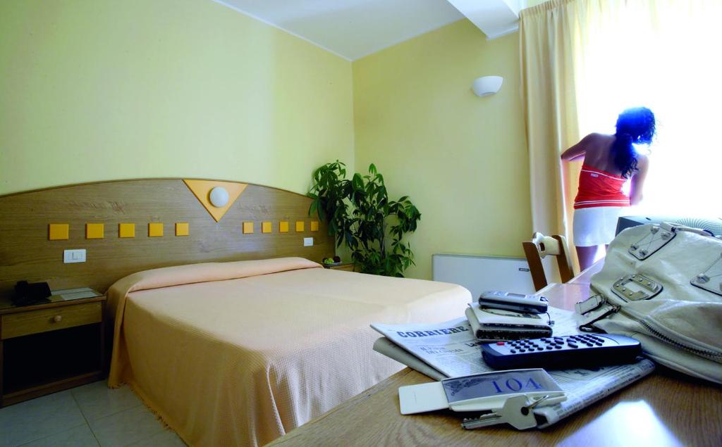 una habitación de hotel con una cama y una mujer mirando por la ventana en Zefiro Residence, en Siderno Marina