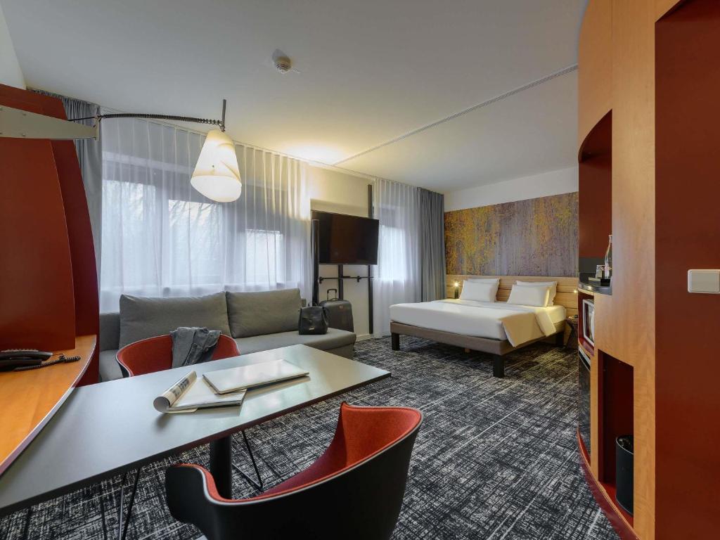 a hotel room with a couch and a table and chairs at Novotel Suites München Parkstadt Schwabing in Munich