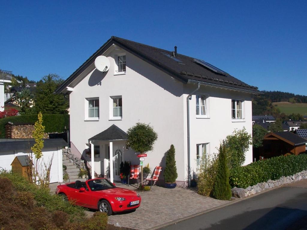 um carro vermelho estacionado em frente a uma casa branca em Ferienwohnung Sommerwind em Willingen