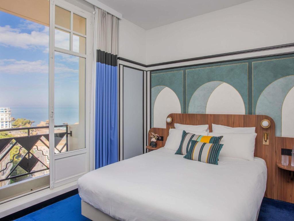 a bedroom with a bed and a large window at Hotel Plaza Biarritz Plage - Handwritten Collection in Biarritz