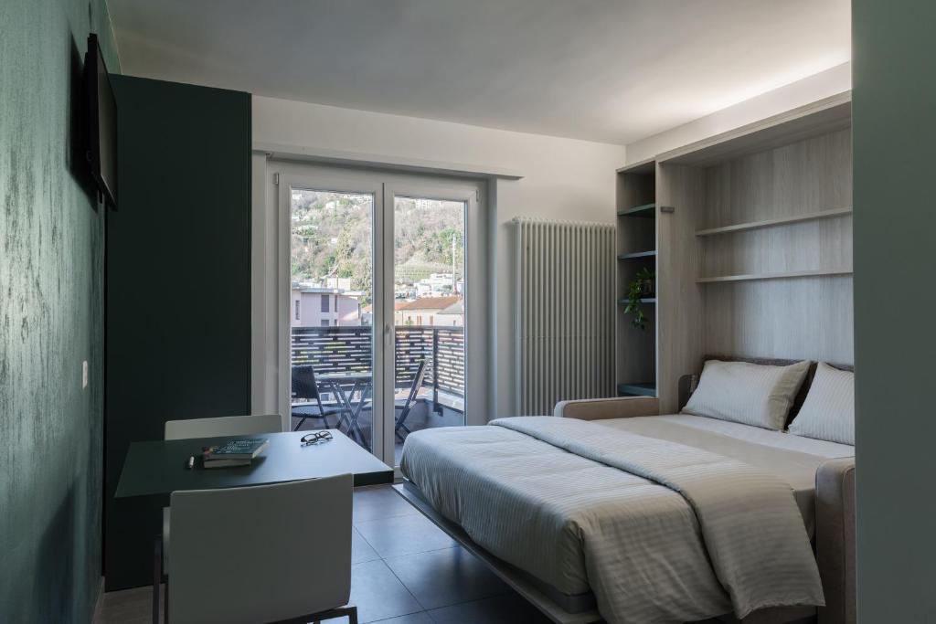 a bedroom with a bed and a desk and a balcony at By THE LAKE in Muralto