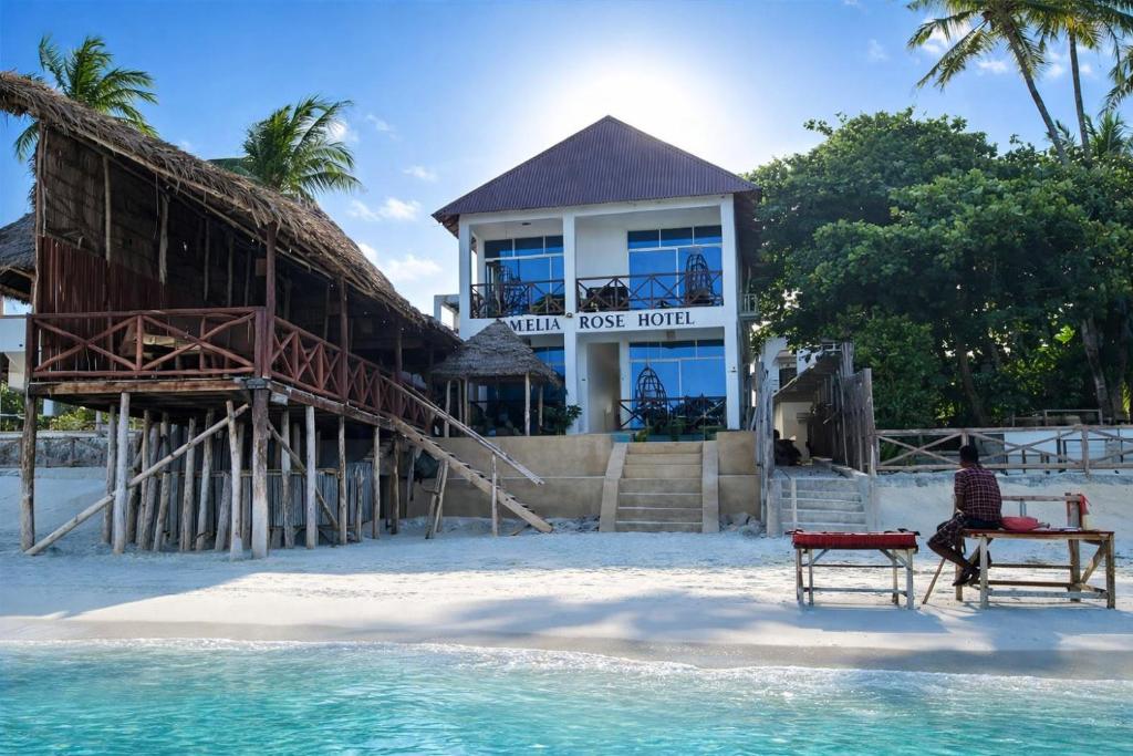 a man sitting on a chair in front of a house on the beach at Aquelia Rose Hotel in Jambiani