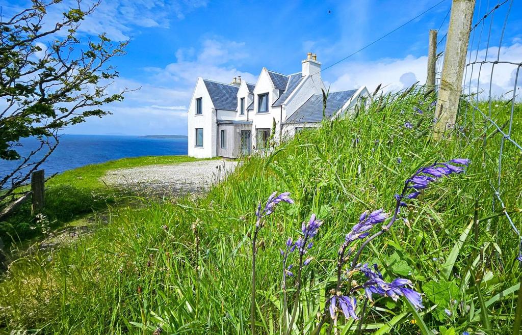 a white house on the side of a hill with purple flowers at Taigh Druim in Elgol