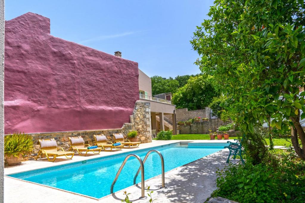 a house with a swimming pool with a purple wall at Villa Verde Petra in Rethymno