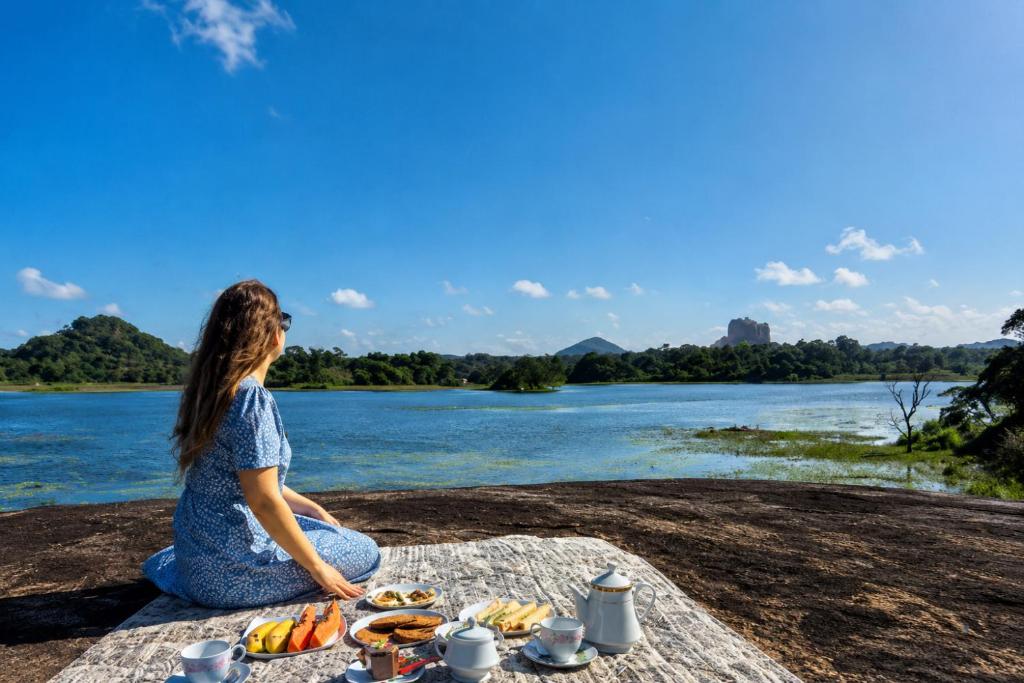 a woman sitting on a table next to a river at Sigiri Lake Paradise in Sigiriya