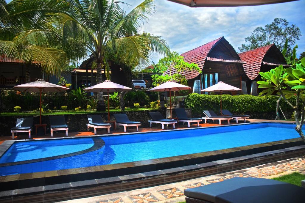 a swimming pool with chairs and umbrellas next to a house at Mamaras Guest House in Nusa Penida
