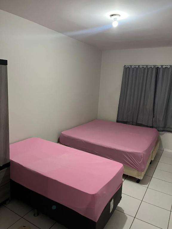 two beds in a room with pink sheets at Quarto para viajantes in Montes Claros