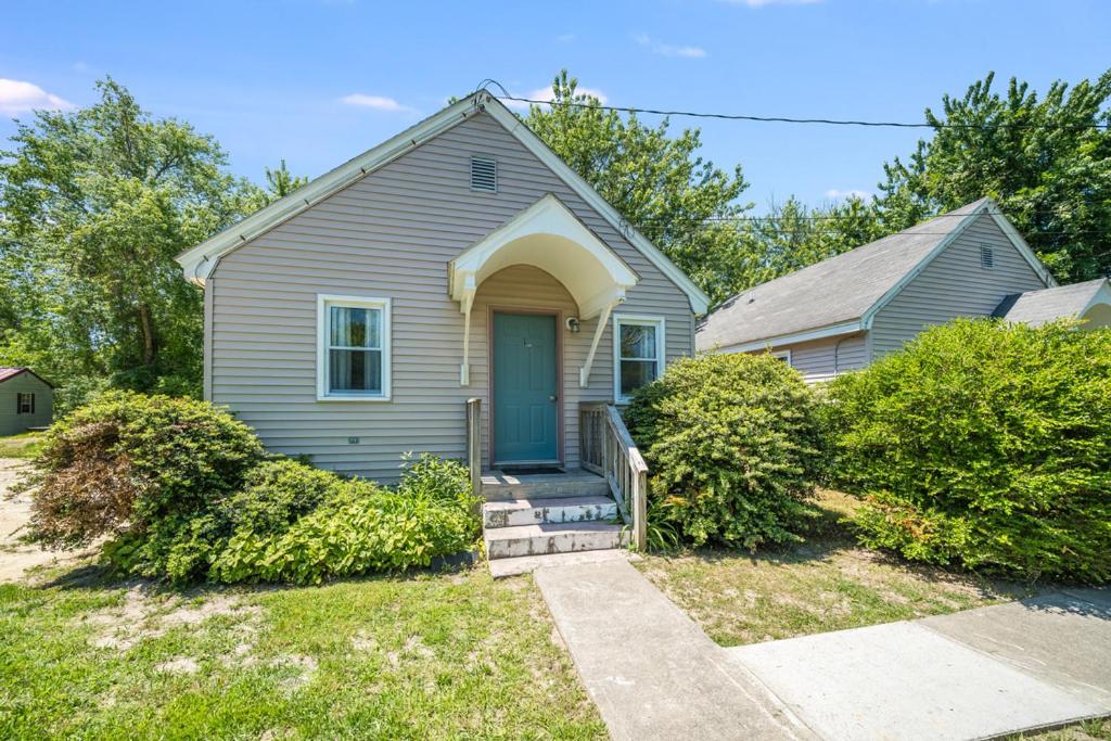 a gray house with a blue door and bushes at Chris Cottage 1 in Chincoteague