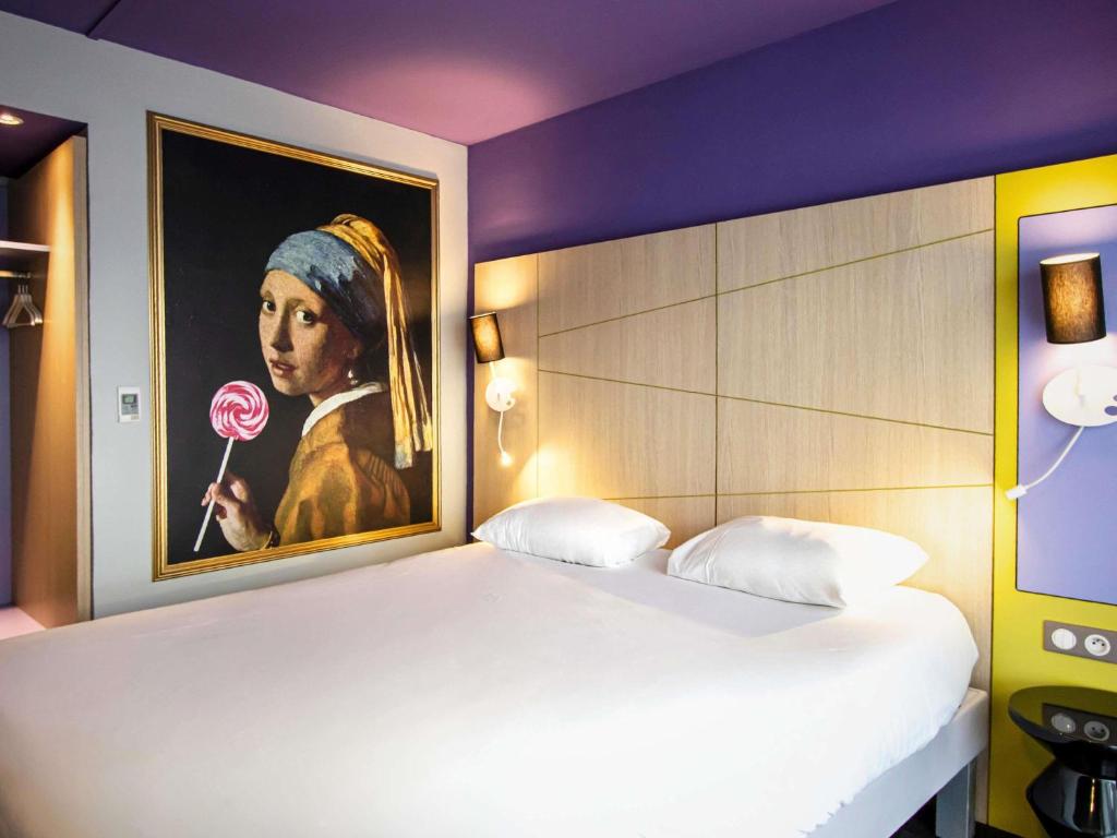 a bedroom with a painting of a woman holding a lollipop at ibis Styles Honfleur Centre Historique in Honfleur