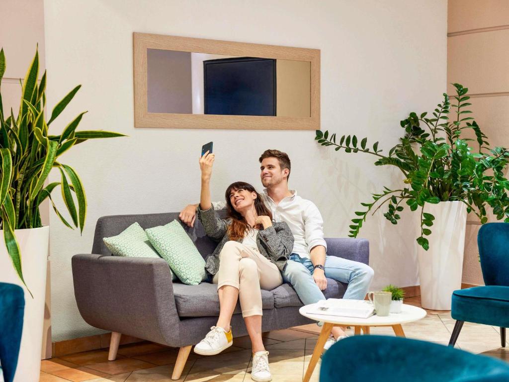 a man and woman sitting on a couch with their hand in the air at Aparthotel Adagio Access Nice Garibaldi in Nice
