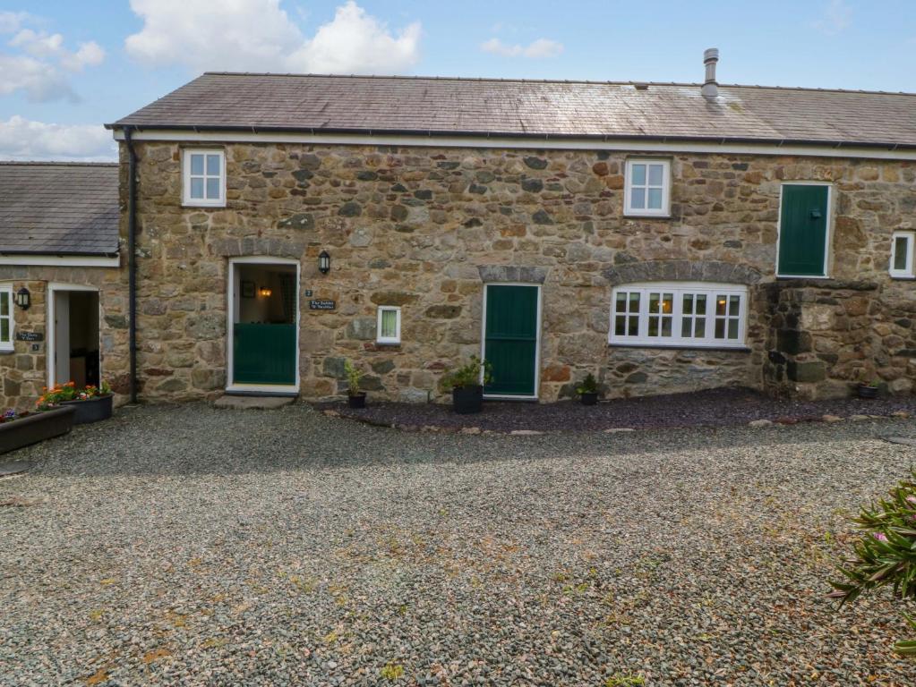 an old stone house with green doors and a gravel driveway at No 2 The Stables in Llangefni