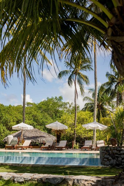 a pool with chairs and umbrellas and palm trees at Villa Cote Sud Pousada De Charme - Pé na Areia in São Miguel dos Milagres