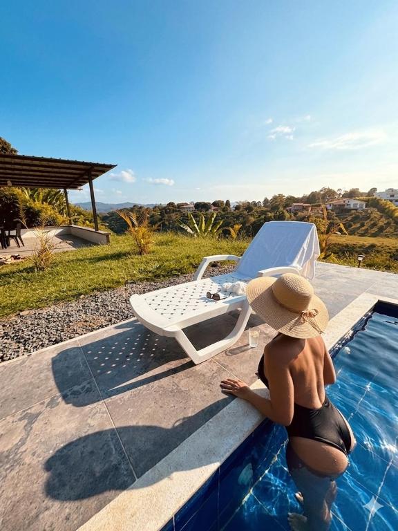 a woman in a hat sitting next to a swimming pool at Finca cerca a Panaca - Birdhouse85 in Alcalá