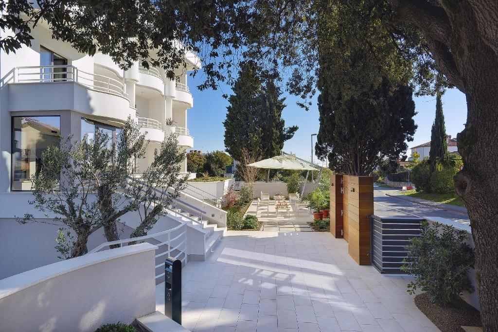 un bâtiment blanc avec des arbres et un trottoir dans l'établissement Residence Rovinj, à Rovinj